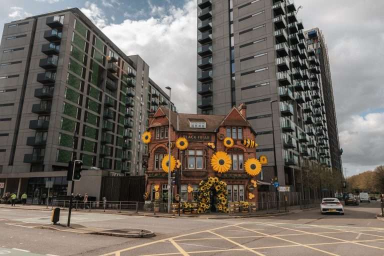 Bright brick pub named Black Friar decorated with large sunflowers in front of modern apartment buildings.