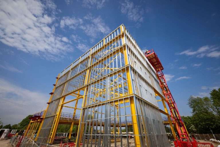 Yellow steel-framed building under construction against a blue sky with a red lifting platform nearby