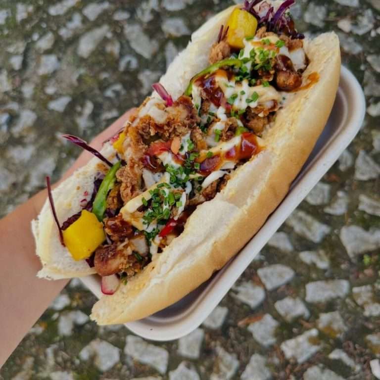 Loaded fried chicken sandwich with crunchy chicken, peppers, greens, and drizzled sauces in a soft bun.