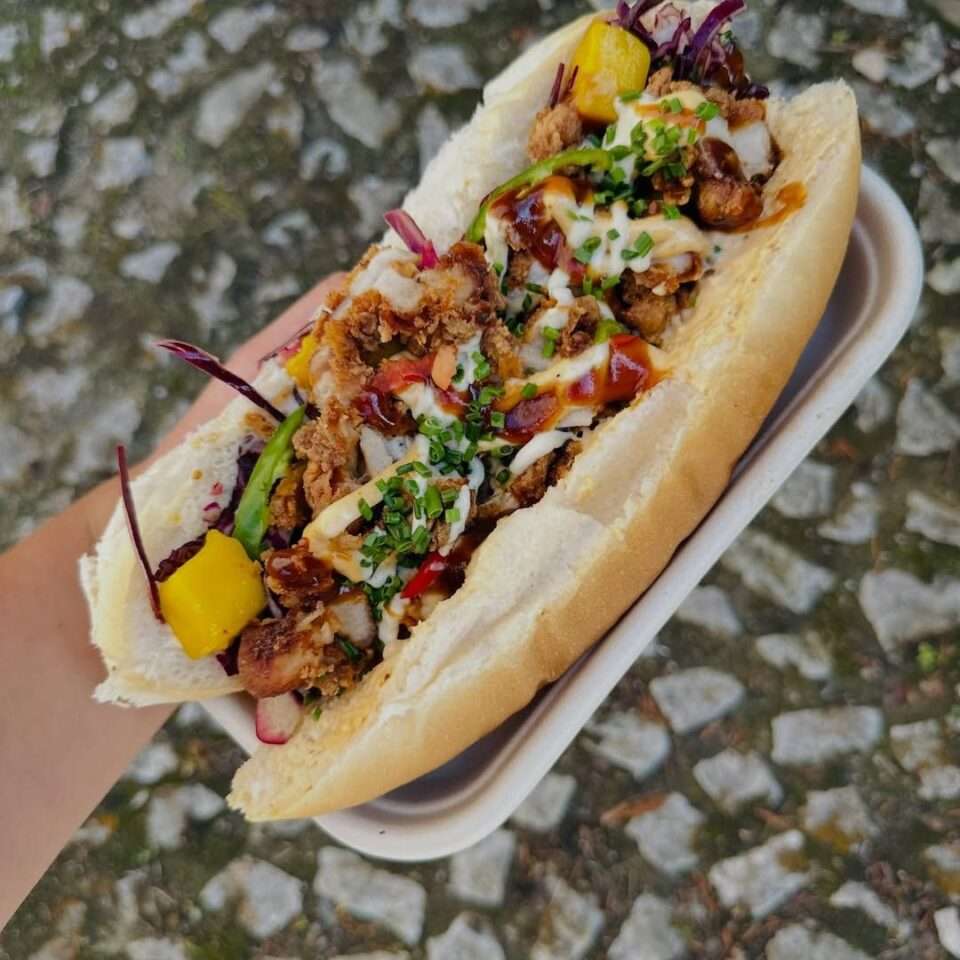 Loaded fried chicken sandwich with crunchy chicken, peppers, greens, and drizzled sauces in a soft bun.
