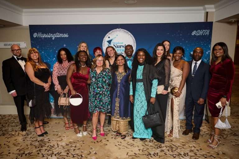 Group of well-dressed students and professionals posing on a blue backdrop at a nursing awards event.