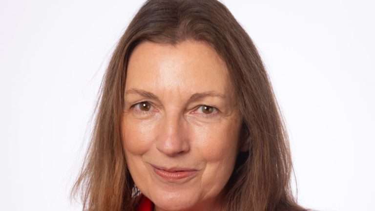 Close-up portrait of a smiling woman with shoulder-length brown hair against a white background, wearing red clothing.