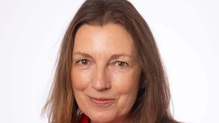 Close-up portrait of a smiling woman with shoulder-length brown hair against a white background, wearing red clothing.