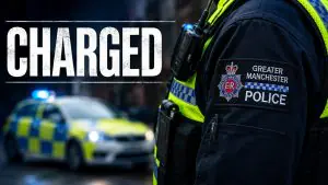 GMP police officer in foreground with a bold 'CHARGED' banner and a police car with blue lights in the background, scene suggesting news.