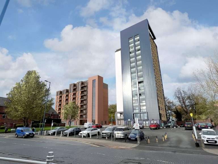 Tall blue-gray glass-clad high-rise next to a brick residential block, with a parking lot and trees under a blue sky.